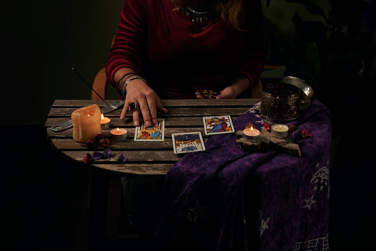 Pythoness reads tarot cards on a table with candles.