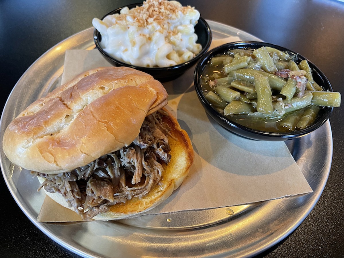 The Smokery's pulled pork is soft and juicy and deeply smoky, falling into thin shreds on a good brioche bun. It's shown with sides of Gouda mac and long-simmered green beans.