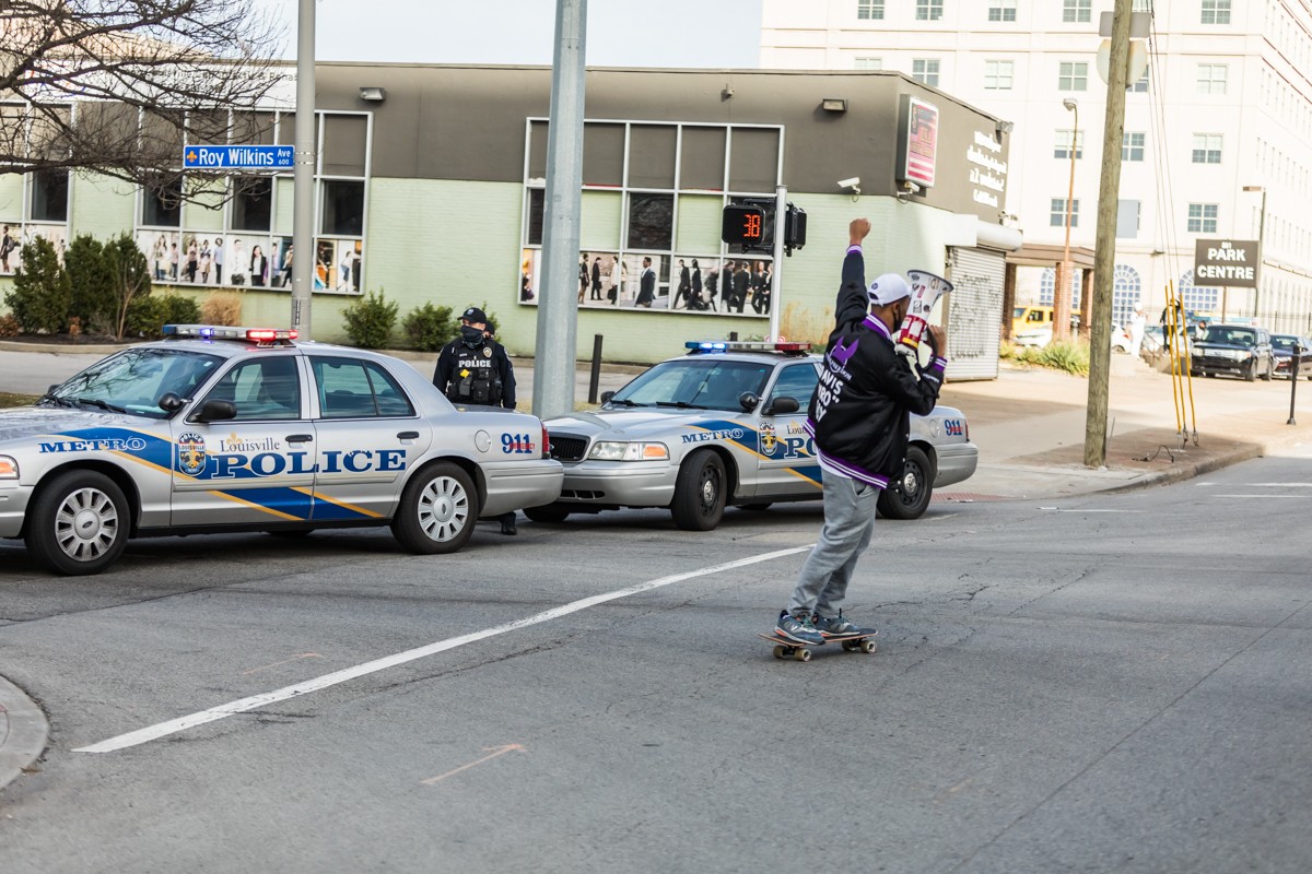 A protester rode by on a skateboard past LMPD vehicles blocking off Roy Wilkins Avenue. - KATHRYN HARRINGTON