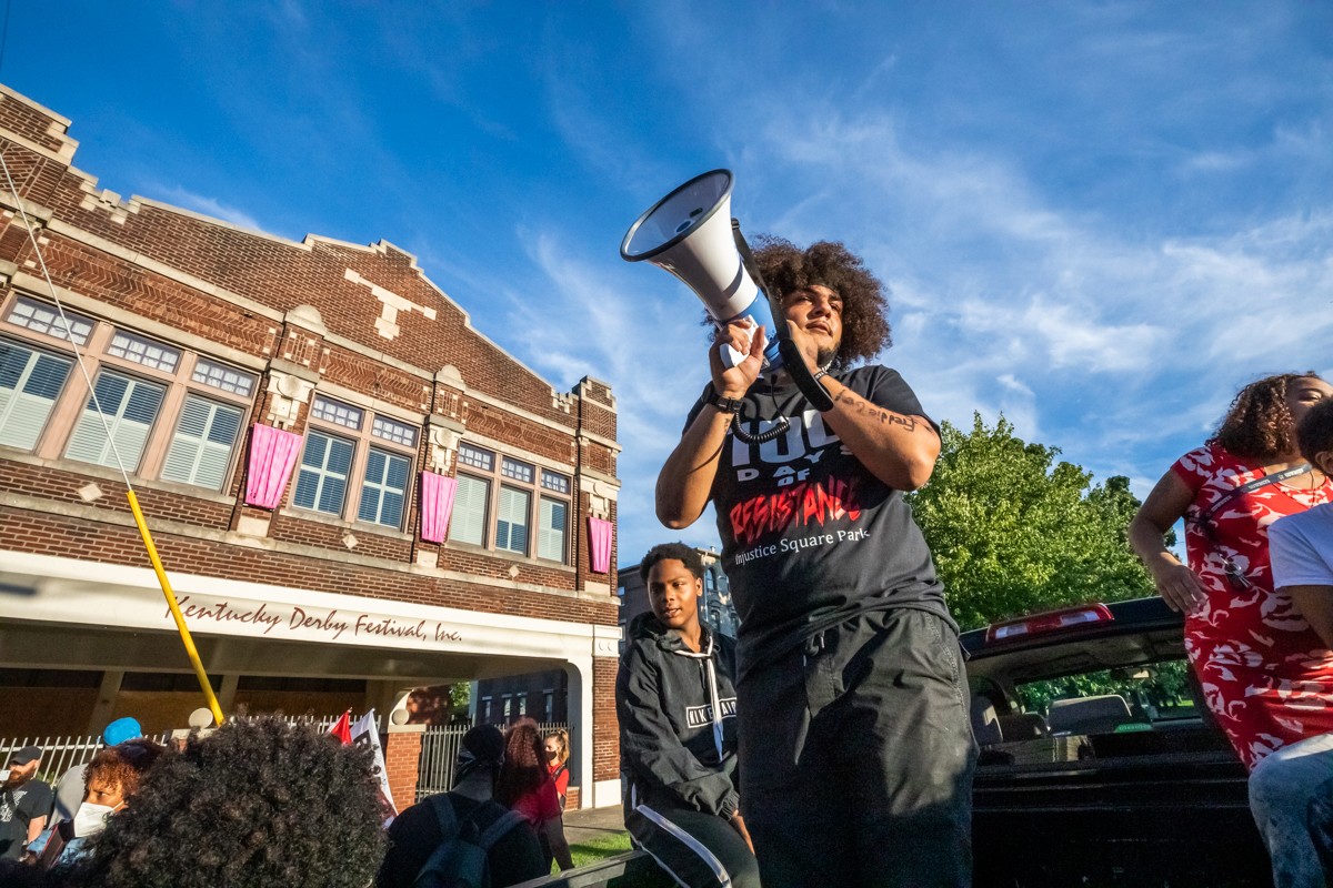 Travis Nagdy spoke to protesters on a megaphone in front of the Kentucky Derby Festival office during a protest. - KATHRYN HARRINGTON