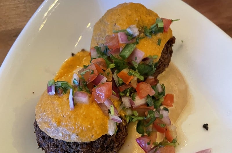 Crunchy on the surface, creamy within, Noosh Nosh's Black bean cakes topped with cashew aioli make an elevated - and tasty - vegan entree.