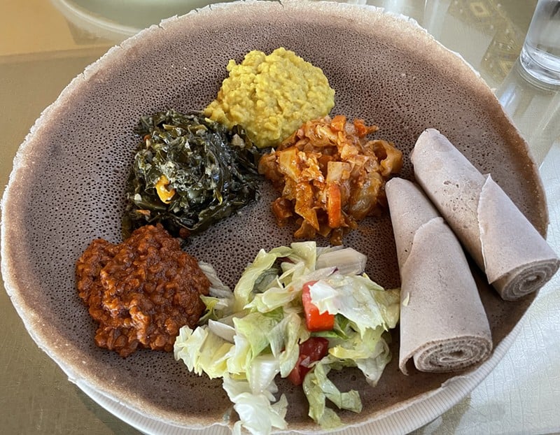 An assortment of four Ethiopian veggie items and a salad on an injera round make up this colorful combination plate.